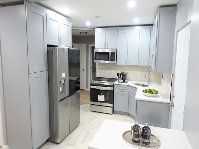 kitchen with gray cabinetry, a sink, marble finish floor, light countertops, and appliances with stainless steel finishes