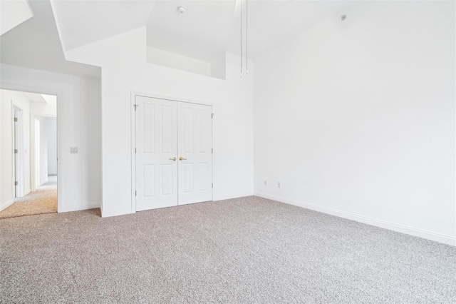 unfurnished bedroom featuring carpet, high vaulted ceiling, and a closet