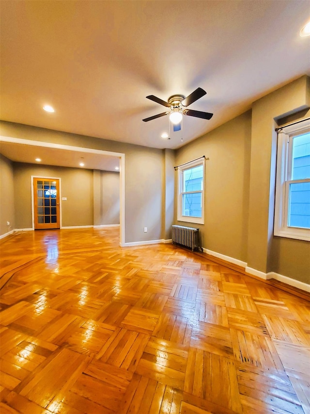 empty room featuring ceiling fan, radiator, and light parquet floors