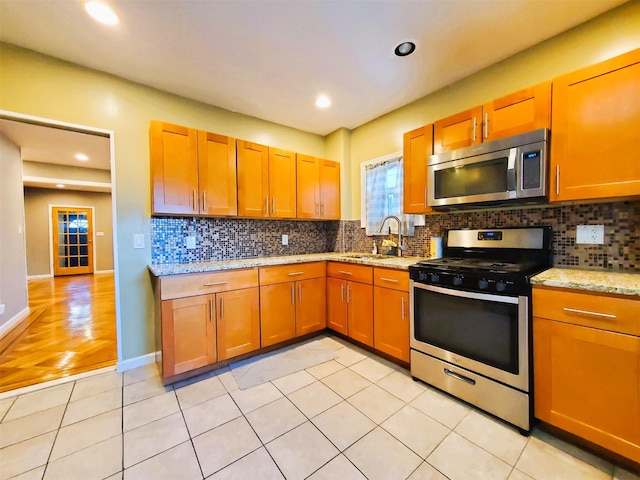 kitchen featuring backsplash, light stone counters, stainless steel appliances, sink, and light tile patterned floors