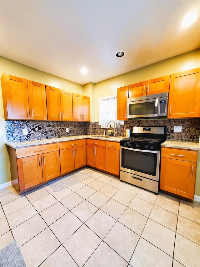 kitchen featuring decorative backsplash, light stone counters, stainless steel appliances, sink, and light tile patterned floors