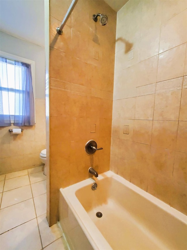 bathroom featuring tile patterned flooring, tiled shower / bath combo, toilet, and tile walls