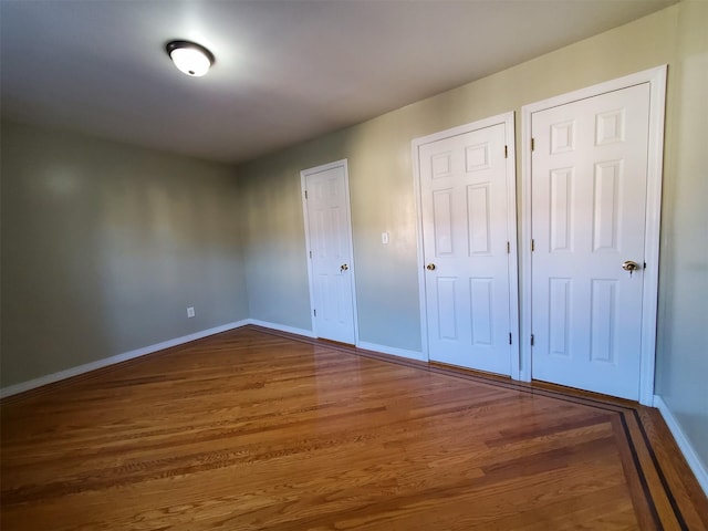 unfurnished bedroom with dark hardwood / wood-style flooring and two closets