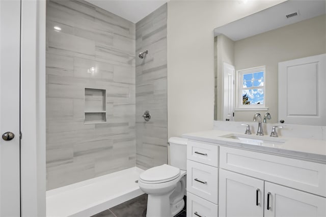 bathroom with vanity, toilet, tile patterned flooring, and a tile shower