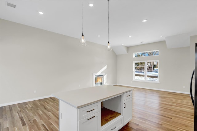 kitchen with a kitchen island, white cabinets, light wood-type flooring, and decorative light fixtures