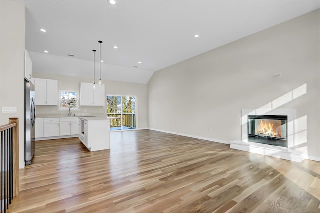 unfurnished living room featuring lofted ceiling, sink, and light wood-type flooring