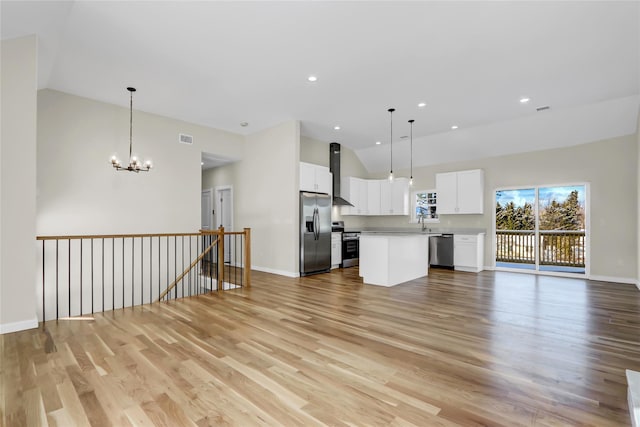 kitchen featuring hanging light fixtures, appliances with stainless steel finishes, white cabinets, and wall chimney exhaust hood