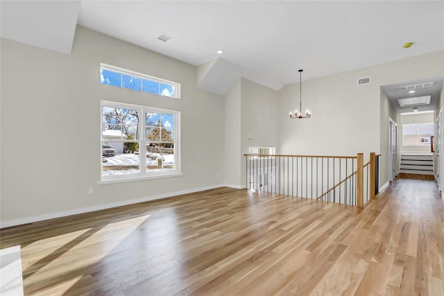 spare room featuring a healthy amount of sunlight, a notable chandelier, and light wood-type flooring