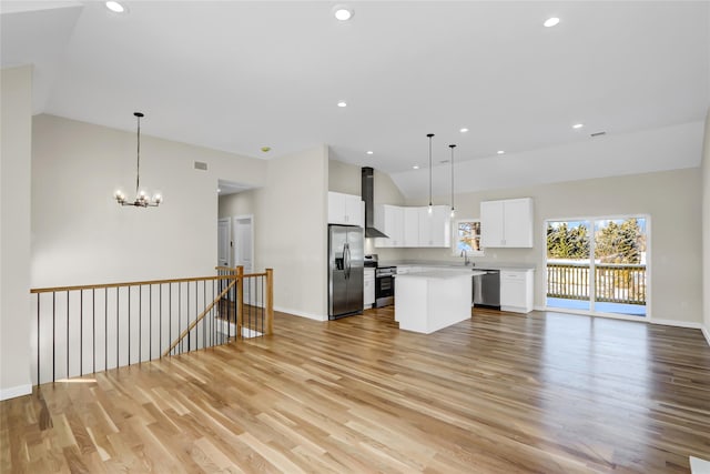 kitchen with decorative light fixtures, a center island, appliances with stainless steel finishes, white cabinets, and wall chimney range hood