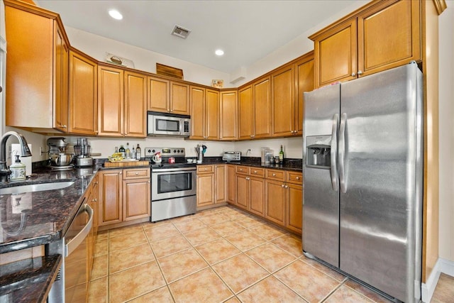 kitchen featuring light tile patterned flooring, appliances with stainless steel finishes, dark stone countertops, and sink