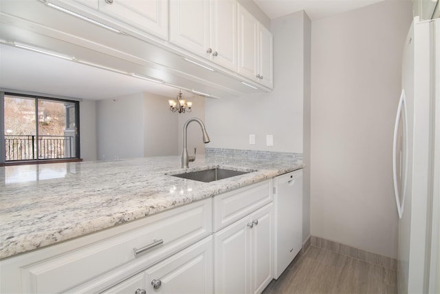 kitchen featuring white appliances, white cabinets, sink, light stone countertops, and a notable chandelier