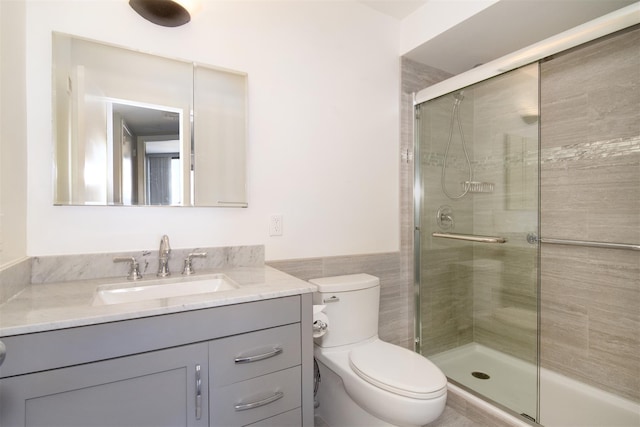 bathroom featuring walk in shower, vanity, toilet, and tile walls