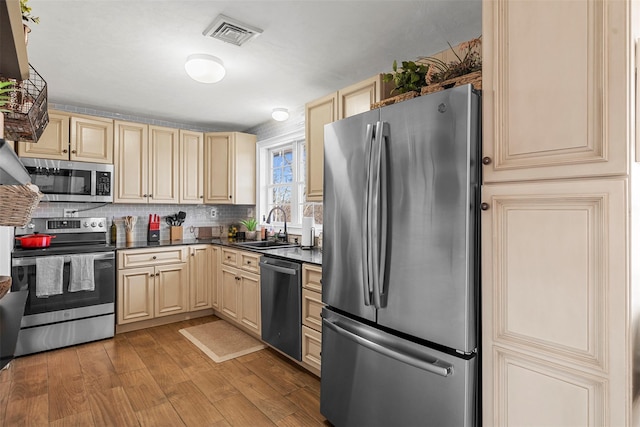 kitchen with appliances with stainless steel finishes, light wood-type flooring, tasteful backsplash, sink, and cream cabinets