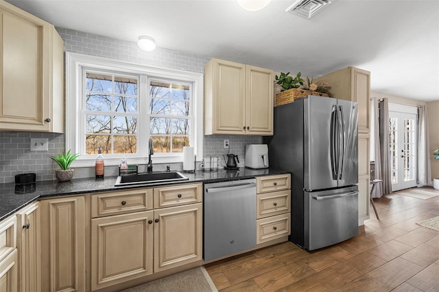 kitchen with sink, backsplash, dark stone countertops, wood-type flooring, and appliances with stainless steel finishes