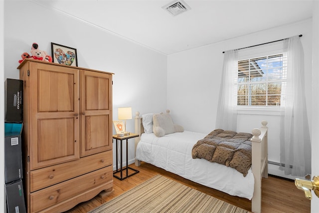 bedroom with light hardwood / wood-style floors and a baseboard heating unit