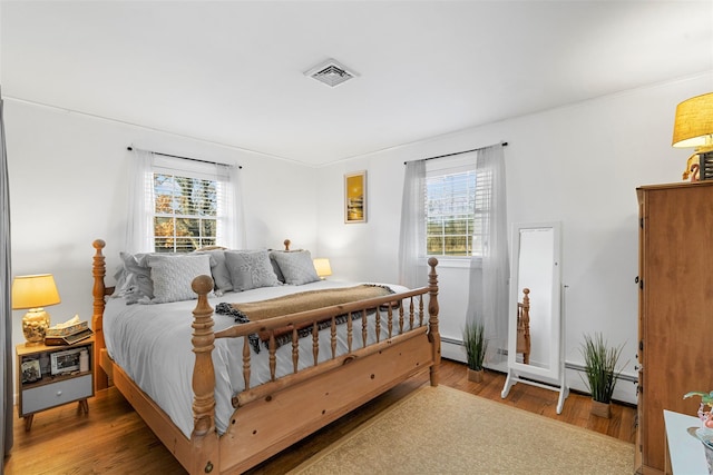 bedroom featuring multiple windows, hardwood / wood-style floors, and a baseboard heating unit