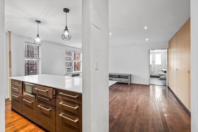 kitchen with dark hardwood / wood-style flooring, dark brown cabinetry, stainless steel microwave, cooling unit, and hanging light fixtures