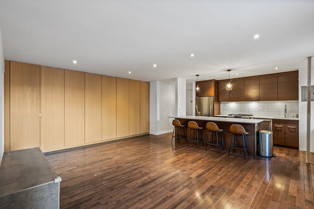 kitchen with dark hardwood / wood-style flooring, backsplash, stainless steel fridge, decorative light fixtures, and a kitchen island