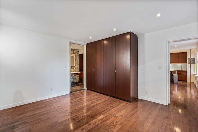 unfurnished bedroom with connected bathroom, a closet, and dark wood-type flooring