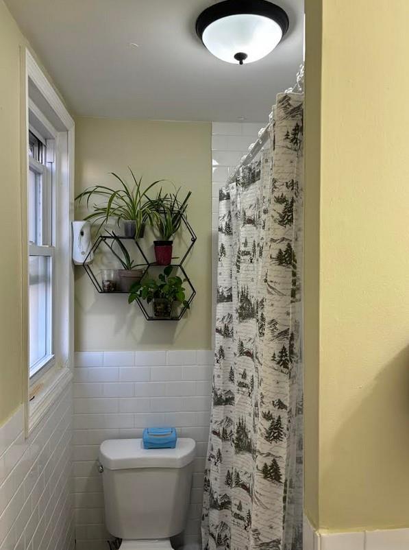 bathroom with a healthy amount of sunlight, toilet, curtained shower, and tile walls