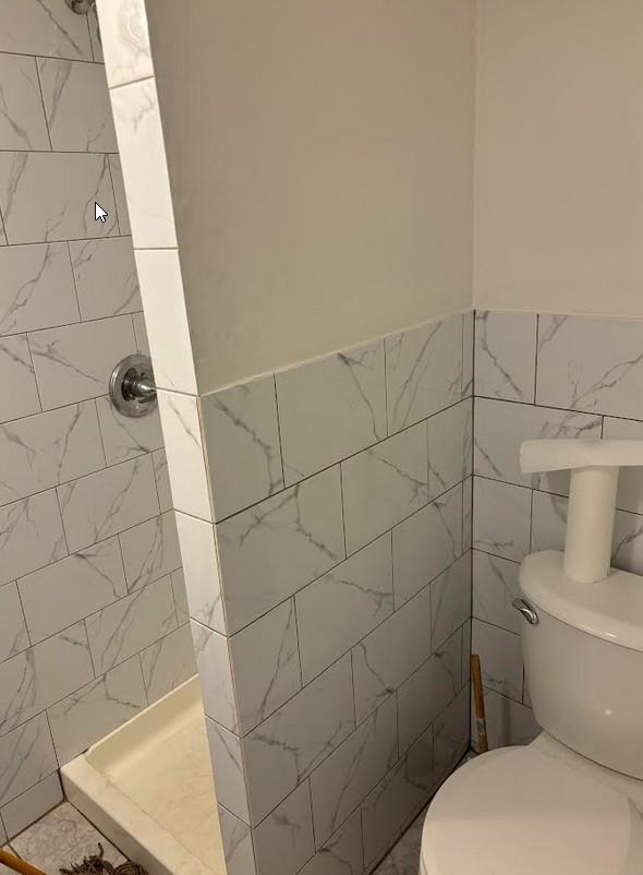 bathroom featuring toilet, a tile shower, and tile walls