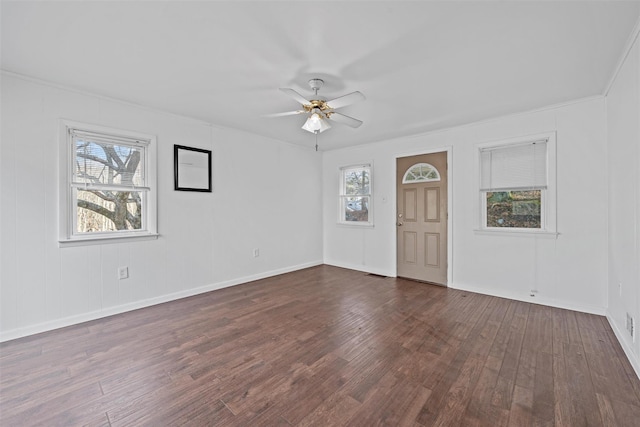 empty room with crown molding, ceiling fan, dark wood-type flooring, and a healthy amount of sunlight