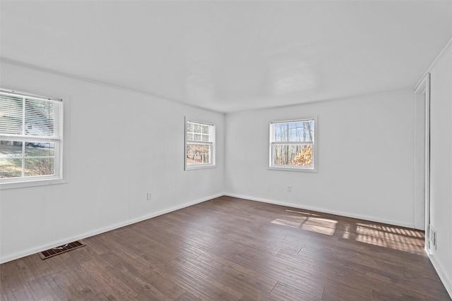 empty room with wood finished floors, visible vents, and baseboards