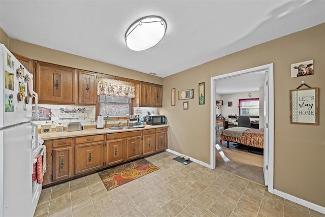 kitchen with light countertops, a sink, freestanding refrigerator, and brown cabinets