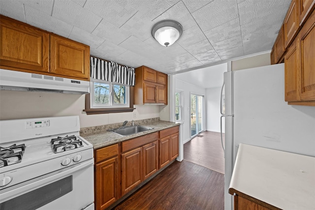 kitchen featuring white appliances, brown cabinetry, a sink, and under cabinet range hood