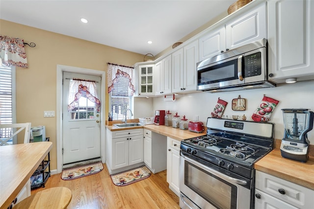 kitchen with wood counters, appliances with stainless steel finishes, sink, light hardwood / wood-style flooring, and white cabinets