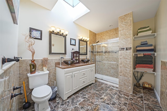 bathroom with a skylight, vanity, a shower with shower door, and tile walls