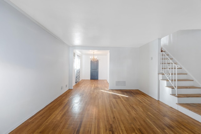 unfurnished living room with hardwood / wood-style flooring, crown molding, and an inviting chandelier