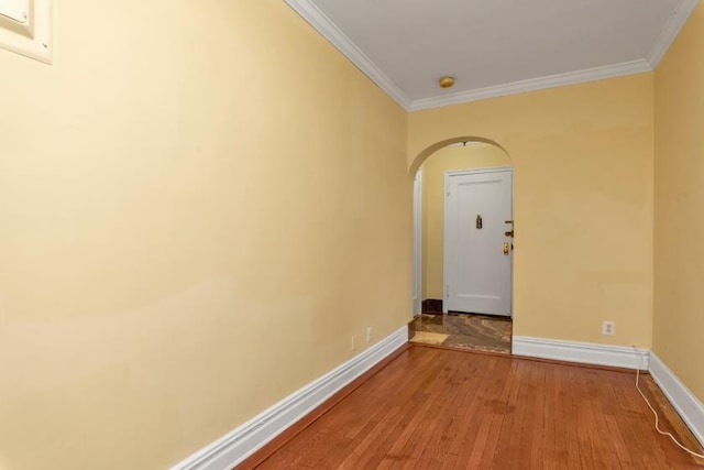 unfurnished room with baseboards, arched walkways, wood finished floors, and crown molding