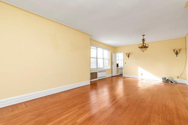 unfurnished room with baseboards, light wood-style floors, and radiator heating unit