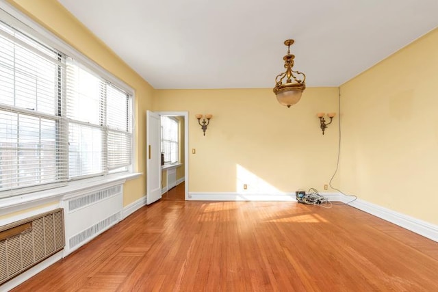 empty room with radiator heating unit, baseboards, and light wood finished floors