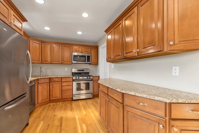 kitchen with light stone counters, stainless steel appliances, light hardwood / wood-style flooring, and sink