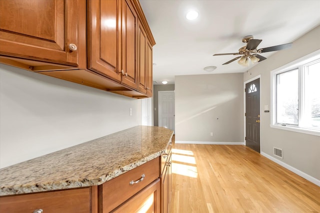 kitchen featuring ceiling fan, light hardwood / wood-style flooring, and light stone counters