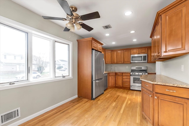 kitchen with appliances with stainless steel finishes, light hardwood / wood-style flooring, ceiling fan, and light stone counters