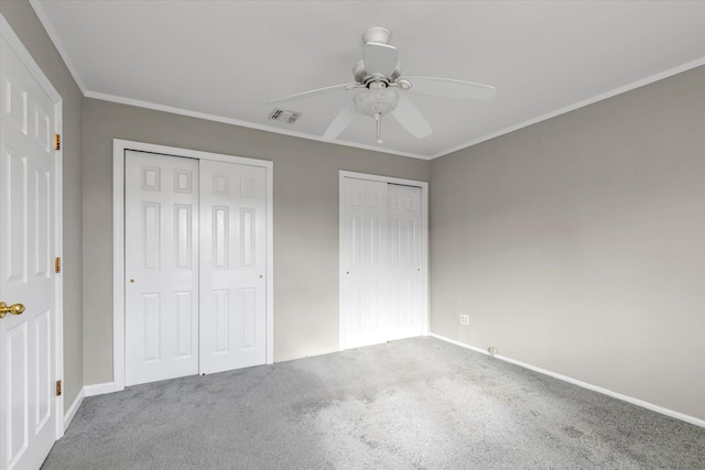 unfurnished bedroom featuring carpet floors, two closets, ceiling fan, and crown molding