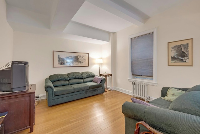 living room featuring beam ceiling, light wood-type flooring, and radiator heating unit