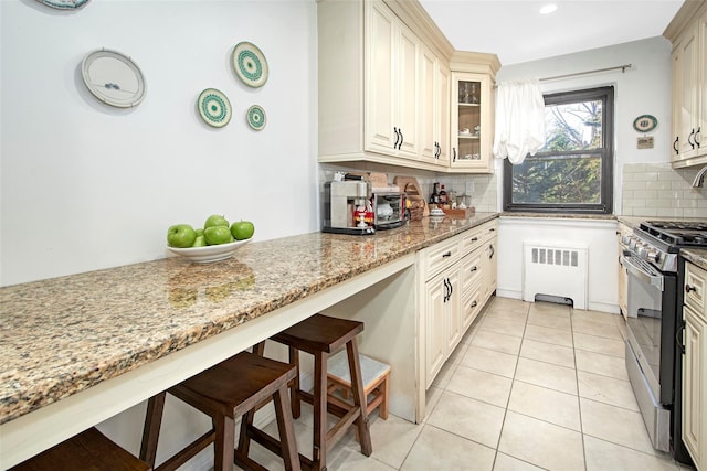 kitchen featuring stainless steel gas stove, light stone countertops, radiator, and tasteful backsplash