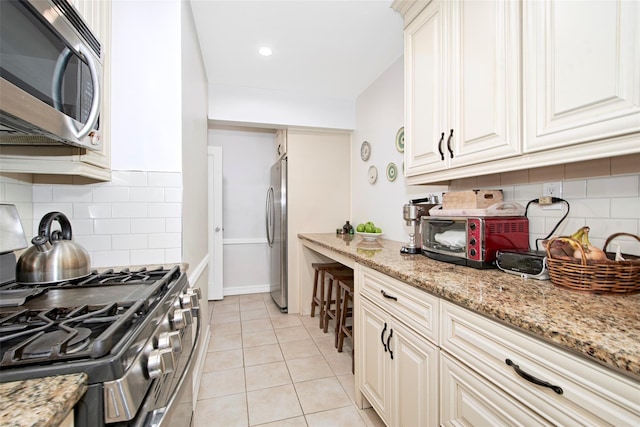 kitchen with decorative backsplash, light tile patterned flooring, light stone countertops, and stainless steel appliances