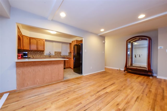 kitchen with kitchen peninsula, decorative backsplash, black fridge, sink, and light hardwood / wood-style flooring