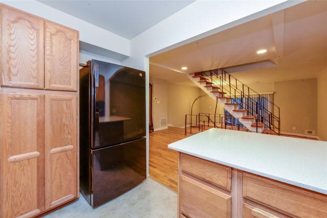 kitchen with light brown cabinetry, black refrigerator, and light hardwood / wood-style flooring