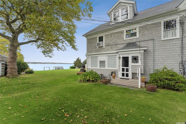 back of property featuring cooling unit, a lawn, a water view, and a shingled roof