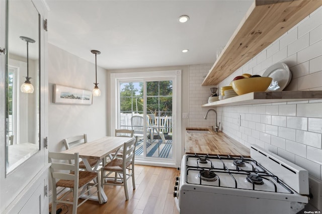 kitchen with light wood finished floors, backsplash, open shelves, white gas range oven, and a sink