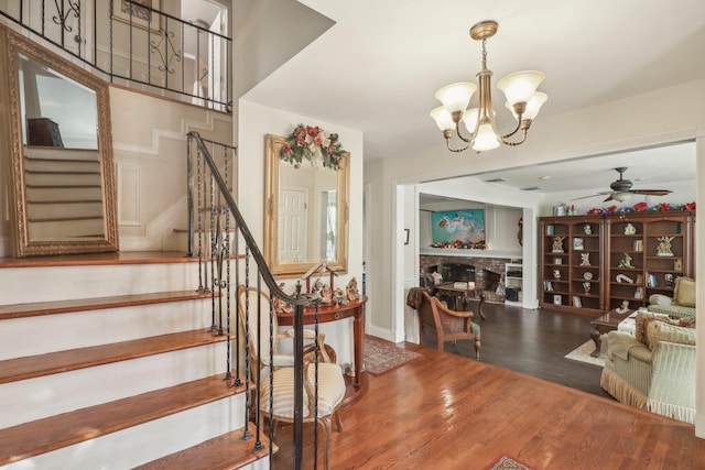 stairs featuring a fireplace, ceiling fan with notable chandelier, and hardwood / wood-style flooring