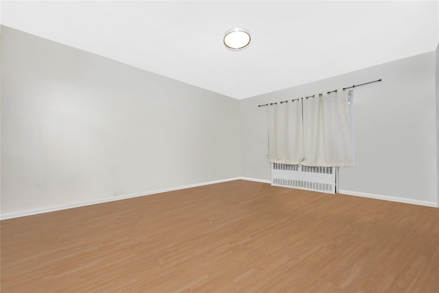 unfurnished room featuring radiator heating unit and hardwood / wood-style flooring