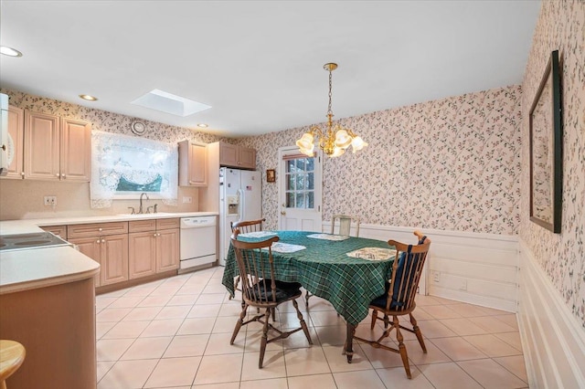 tiled dining area featuring a skylight, a wealth of natural light, sink, and a chandelier