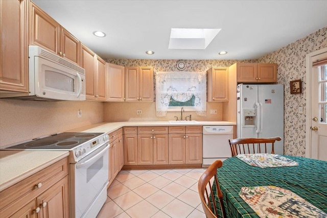 kitchen with light brown cabinetry, a skylight, white appliances, sink, and light tile patterned flooring